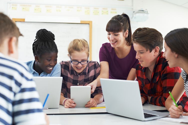 Teacher and teenagers using tablet and laptops.