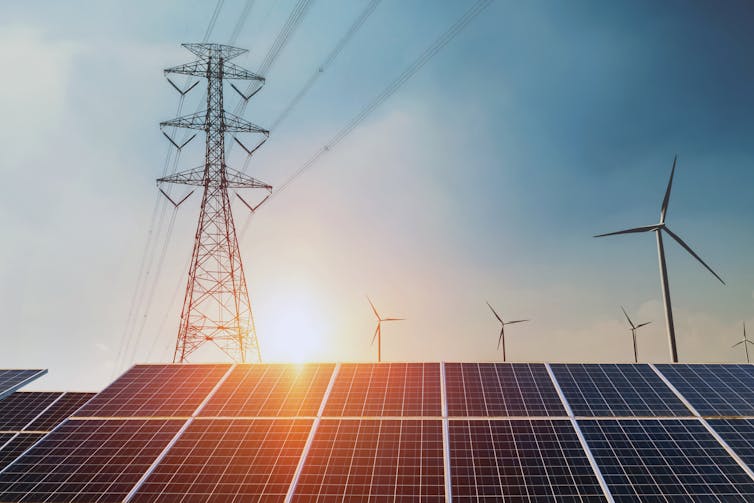 Solar panels with wind turbines and a pylon in the background.