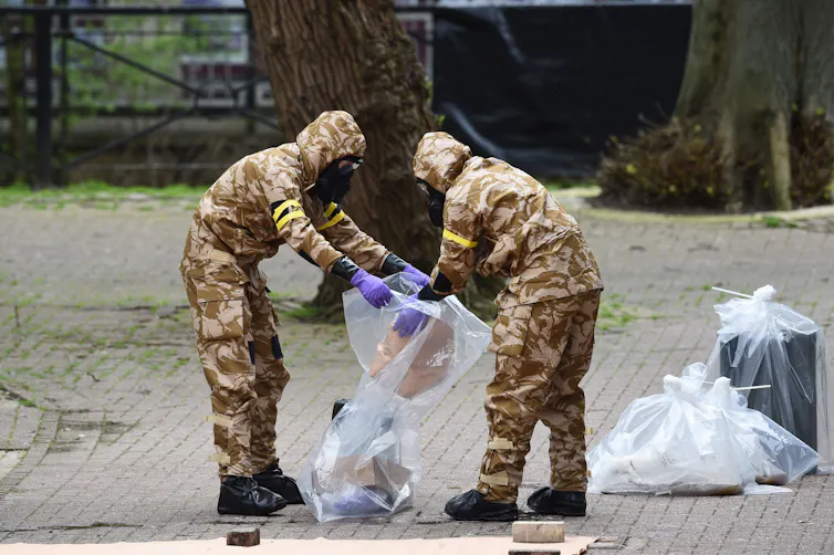 Men in army uniform putting contaminated material in plastic bag