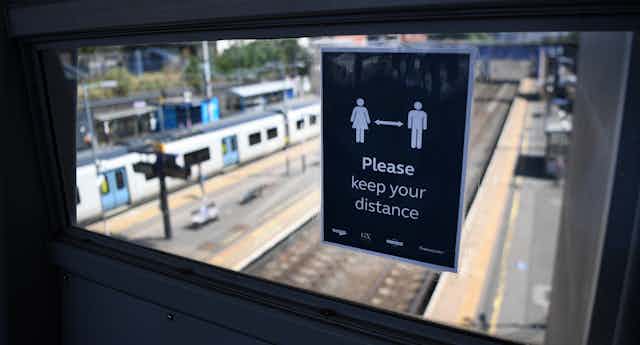A sign at a railway station asks the public to remain physically distant