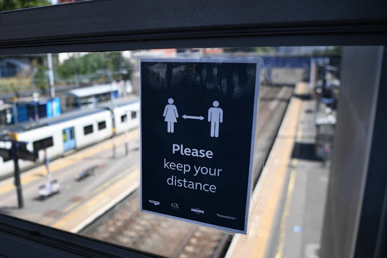 A sign at a railway station asks the public to remain physically distant
