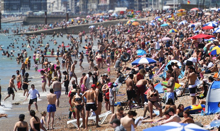 Thousands of people sunbathing and swimming in the sunshine at Brighton beach.
