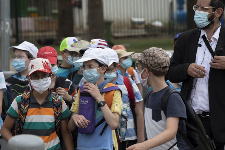 Children wearing face masks walk close together with an adult
