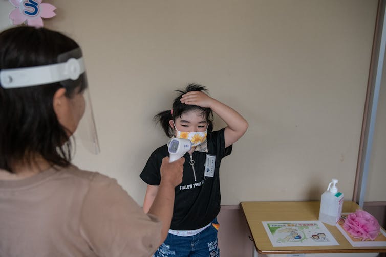 Nurse in protective gear takes the temperature of a small child