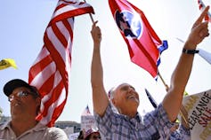 Two middle-age white men wave flags against a blue sky