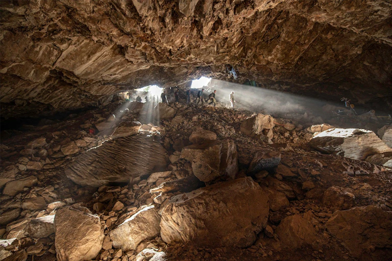 Three people descending into a cave.