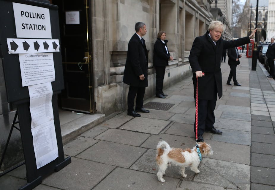 Boris Johnson waving with dog next to sign saying polling station