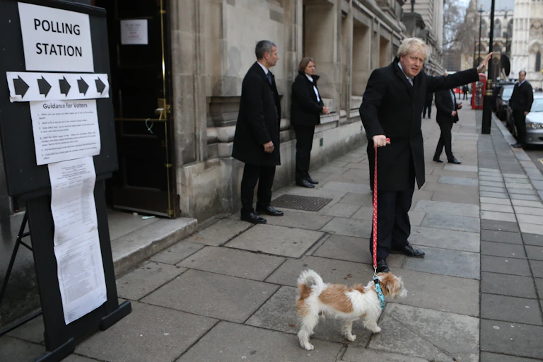 Boris Johnson waving with dog next to sign saying polling station