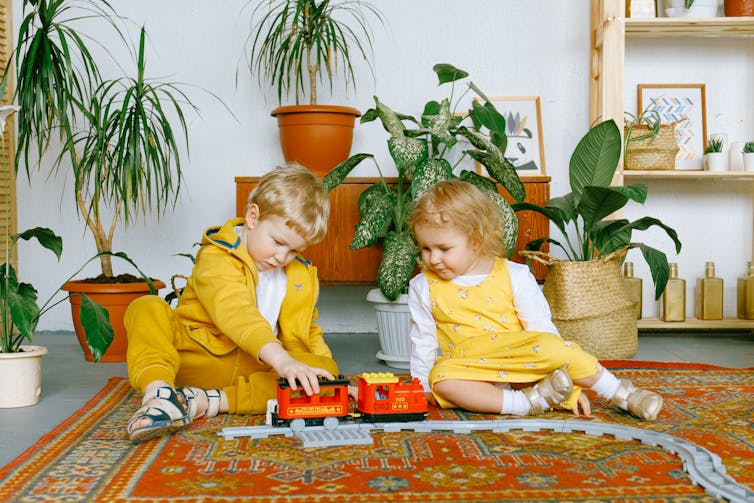 Little boy and girl sitting on the floor playing with toy train set.