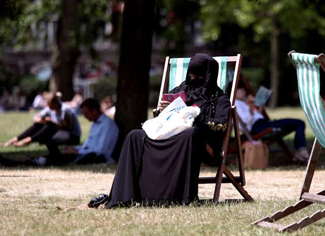 Woman in a burqa sits on a deck chair in a park