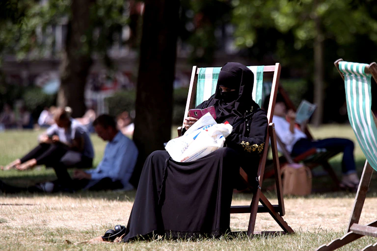 Woman in a burqa sits on a deck chair in a park