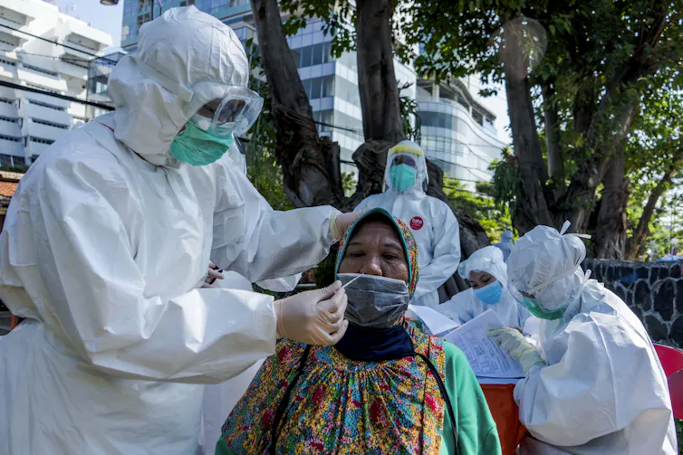 An Indonesian woman is swabbed for a coronavirus test by a man in a hazmat suit.