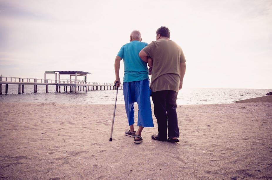 'Son helps his elderly father walk on the beach'