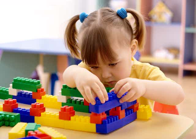 Preschool-age girl playing with plastic building bricks.