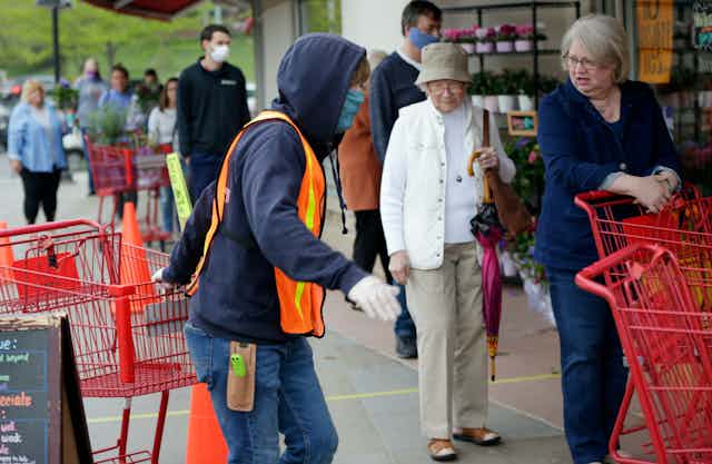 Doorman Dilon Moore, center, helps with shopping carts and controls the number of customers allowed to shop at one time at a Trader Joe's supermarket in Omaha, Neb., on May 7. 