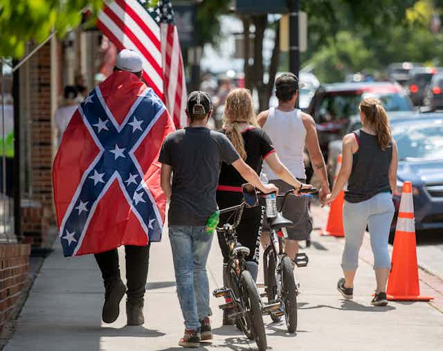 Man draped in Confederate flag walks down street with others