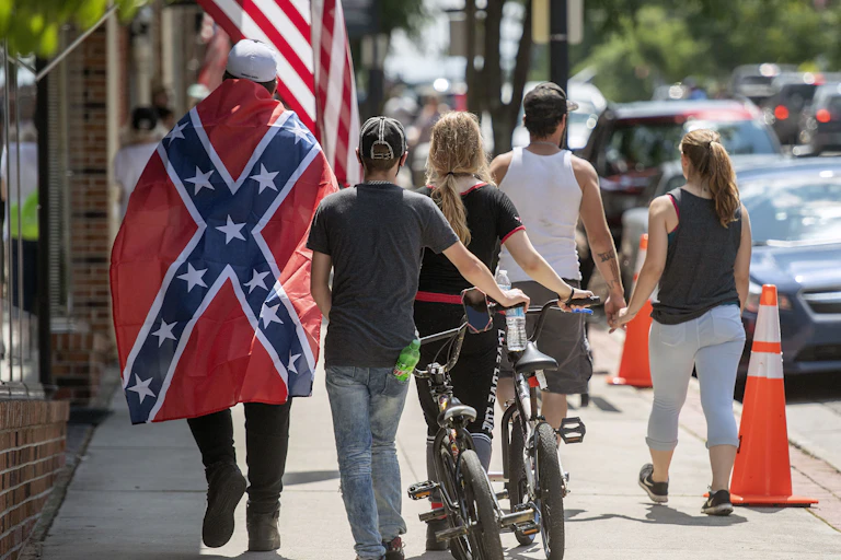 Man draped in Confederate flag walks down street with others