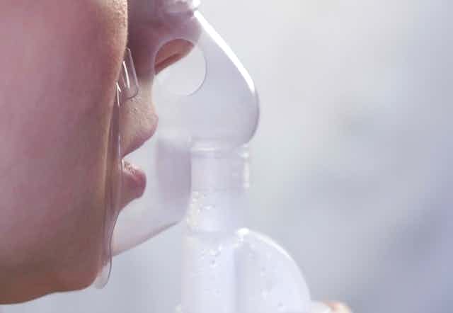 A woman inhales a drug through a nebuliser.