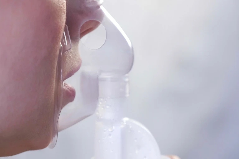 A woman inhales a drug through a nebuliser.