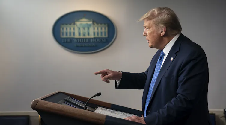Trump, in profile, points his finger from behind a podium as he speaks at a news conference with the White House seal on the wall in the background.