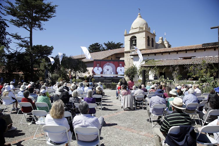 A crowd watches Pope Francis on a screen outside a Spanish colonial building