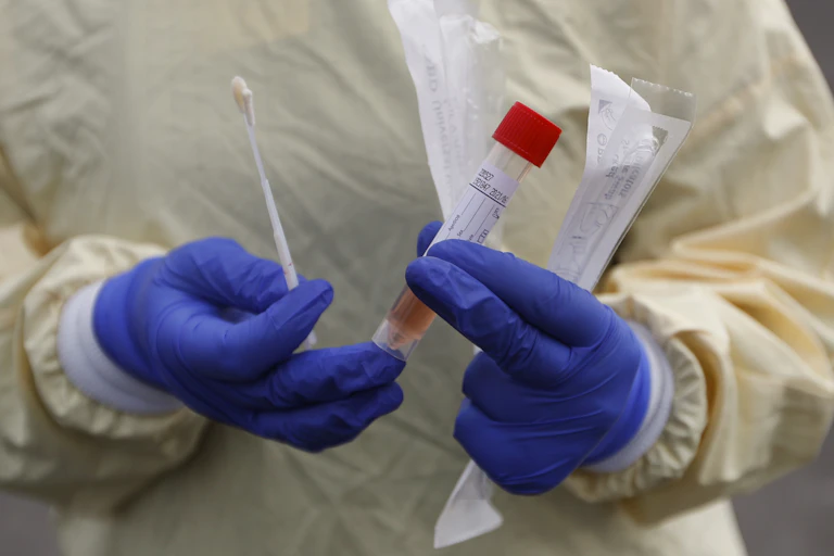 A nurse holding a swab and test tube at a testing station in Michigan