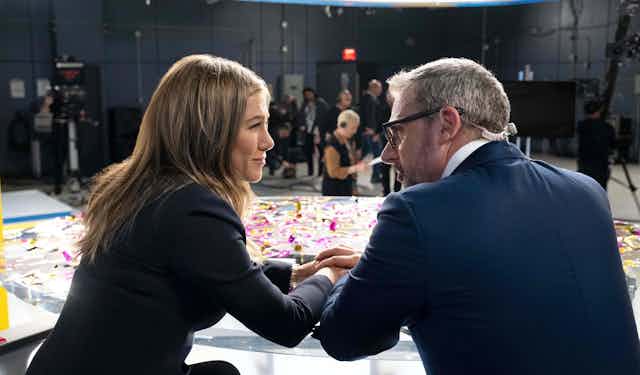 Jennifer Aniston and Steve Carell in role as news anchors hold hands in a still from 'The Morning Show.'