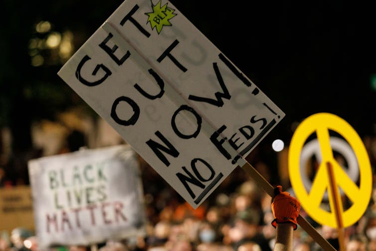 A person holds a banner saying 'GET OUT NOW! NO FEDS!' at the Mom's March near the Justice Center in Portland, Oregon, on July 21, 2020.