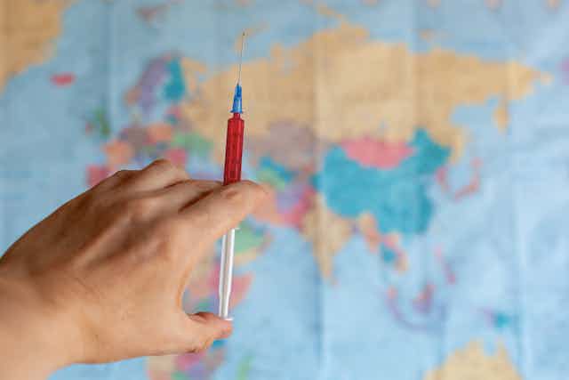 Hand holding syringe in front of world map