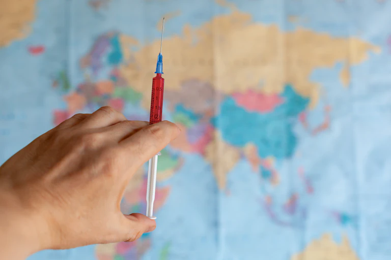 Hand holding syringe in front of world map