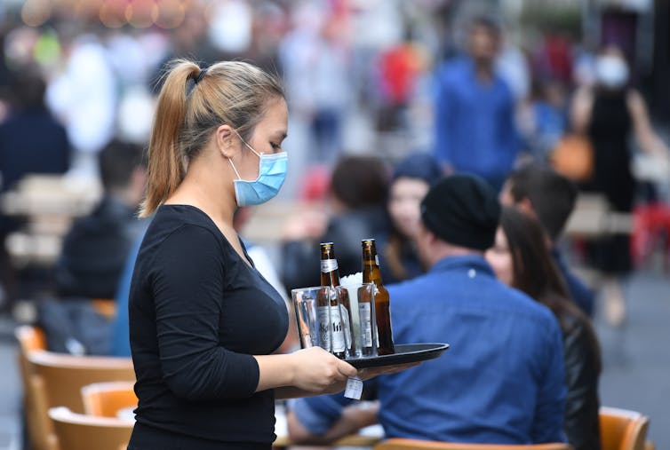 A waitress wearing a facemask serving drinks at a bar.