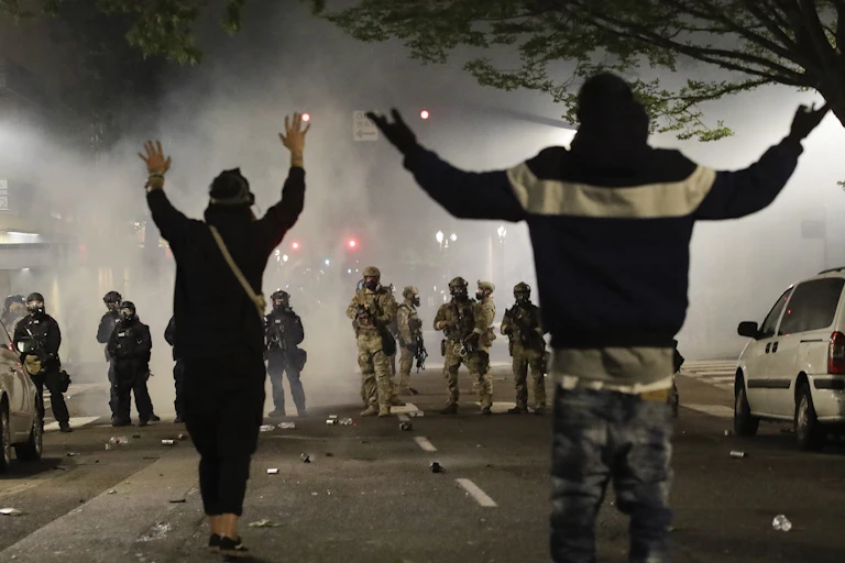 Demonstrators stand in front of federal officers with their hands raised during a Black Lives Matter protest