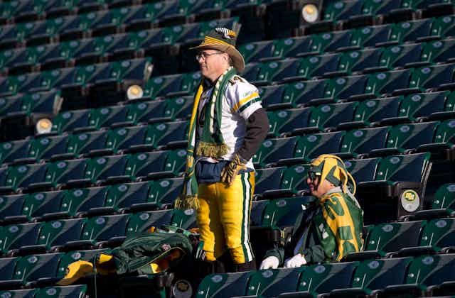 Two fans of Edmonton's CFL team in the stands watching a team practice, while wearing team merchandise.