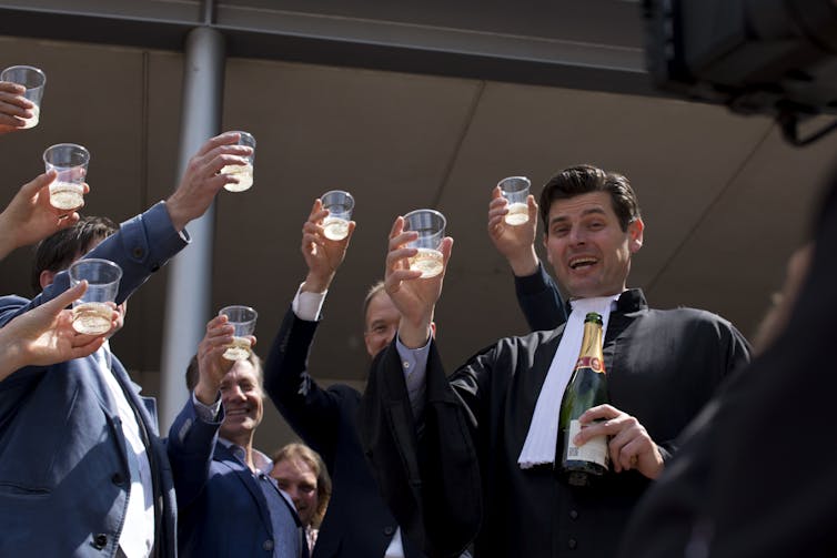 Four people hold up plastic cups with champagne, toasting to their court victory.