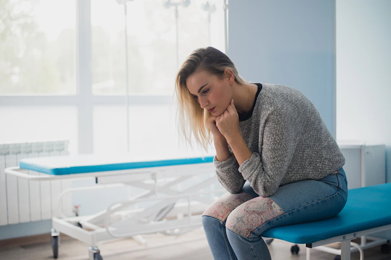 Young woman sitting on hospital bed slumping her head into her hands.