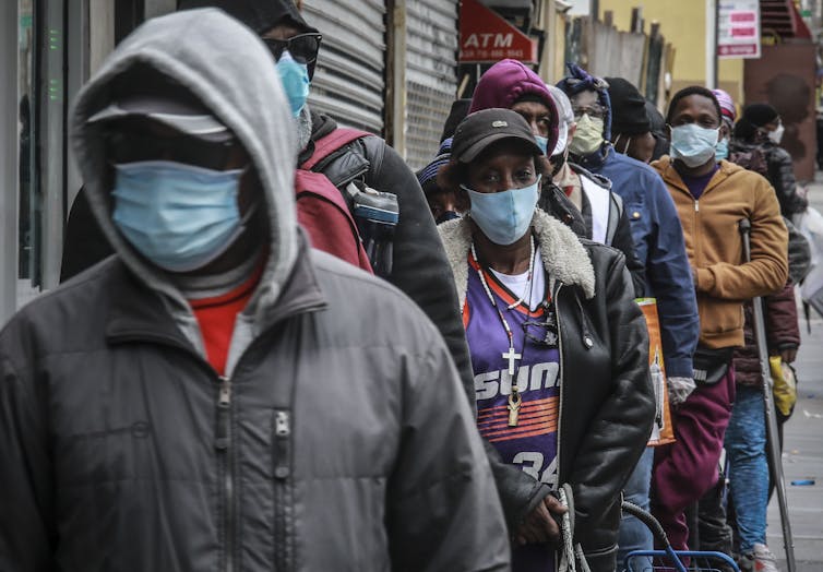 A number of African Americans lining up in the street wearing masks.