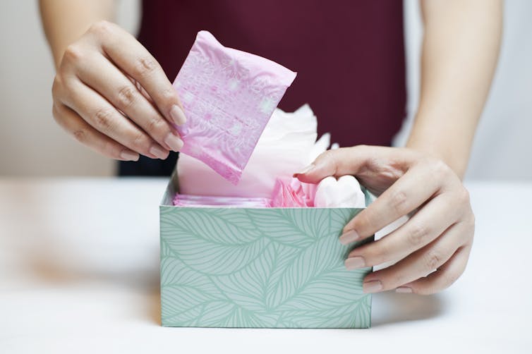 A woman choosing a sanitary pad from a box containing sanitary items.