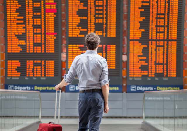A man stands before an airport departure board.