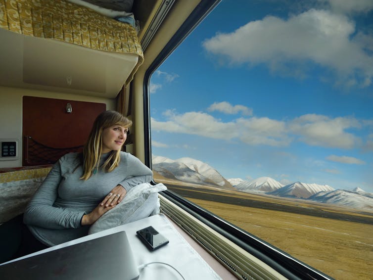 A woman stares out at the Tibetan plains while propped up on a pillow in a sleeper train carriage.