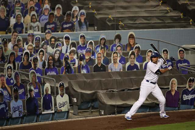 A baseball player swings a bat in front of stadium seats filled with cutouts of fake fans.