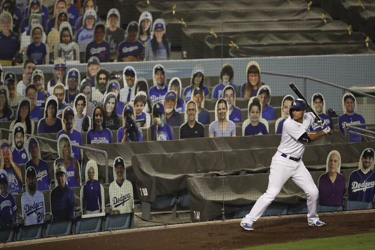 A baseball player swings a bat in front of stadium seats filled with cutouts of fake fans.