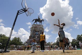 Una giovane ragazza di colore gioca a basket in un campo improvvisato di fronte alla statua di Robert E. Lee, coperta di graffiti antirazzisti, a Richmond, Va.