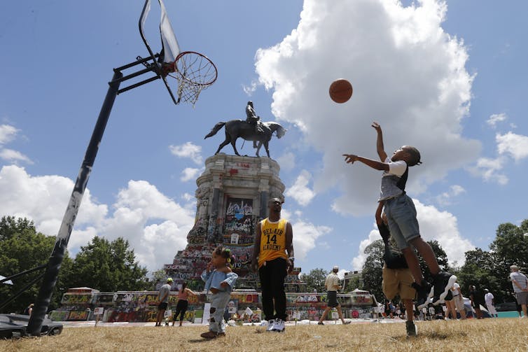 A young Black girl plays basketball at a makeshift court in front of the Robert E. Lee statue, covered in anti-racist graffit, in Richmond, Va.