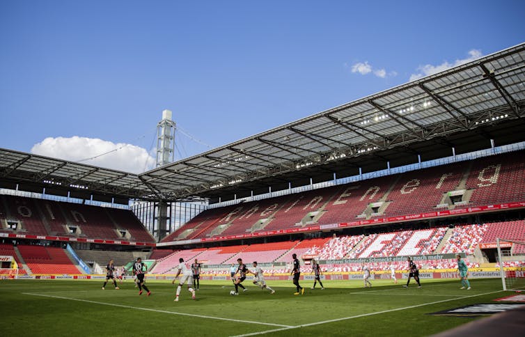 German soccer players fight for the ball in an empty stadium.