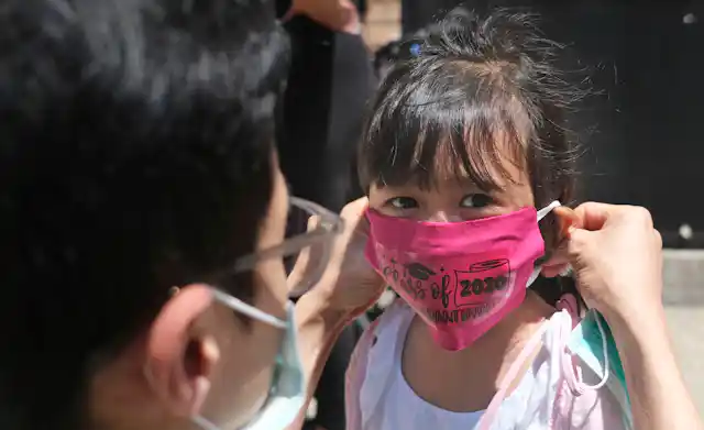 A father puts a pink face mask on his young daughter.