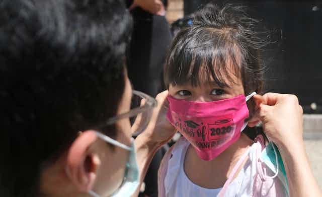 A father puts a pink face mask on his young daughter. 
