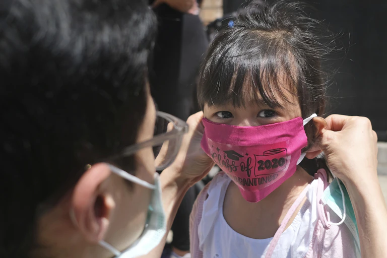A father puts a pink face mask on his young daughter.