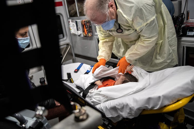 A doctor in personal protective gear treating a young child inside of an ambulance.