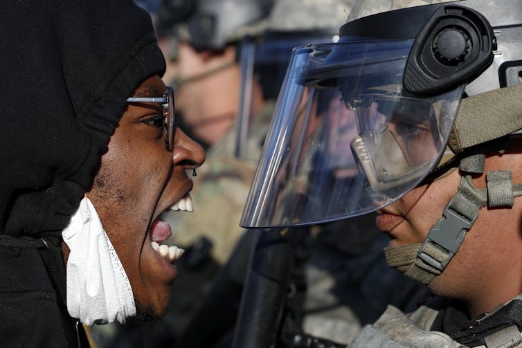 A Black protestor shouts at a national guardsman, wearing fatigues and a face shield, during a protest