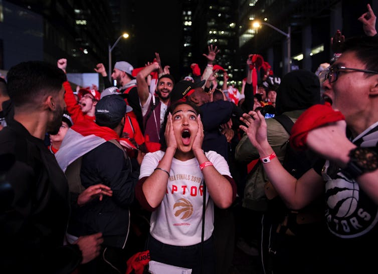 Fans cheer and celebrate the Toronto Raptors victory outdoors at night.